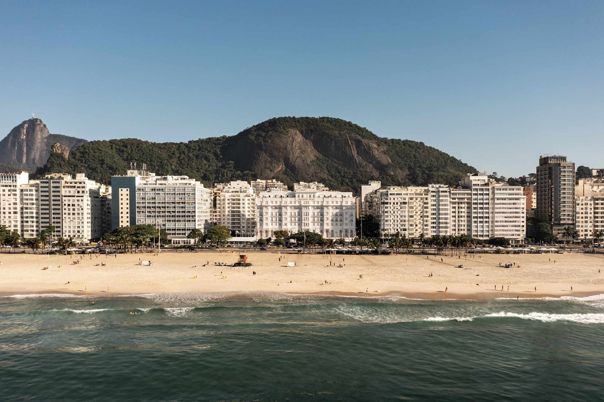 Copacabana beach seen from the sea, with the white façade of the Copacabana Palace among the seafront buildings and the hills behind