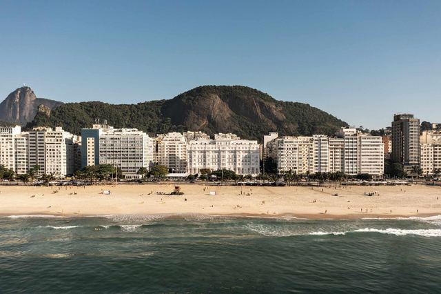Copacabana beach seen from the sea, with the white façade of the Copacabana Palace among the seafront buildings and the hills behind